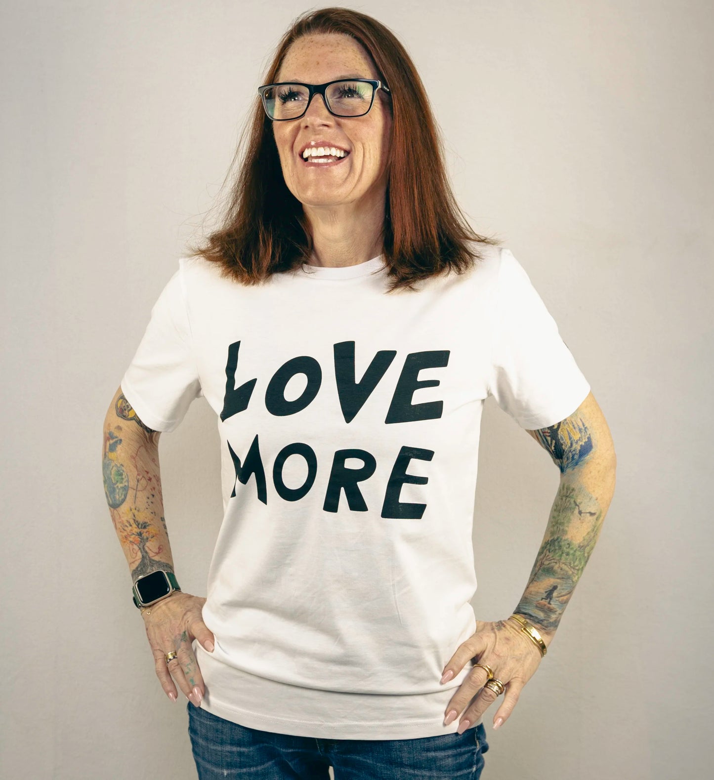 A smiling person wearing a white t-shirt with the text 'LOVE MORE' printed in black.