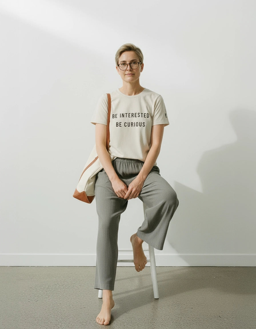 woman wearing a ponlo.com t-shirt with text, sitting on a stool against a white wall.