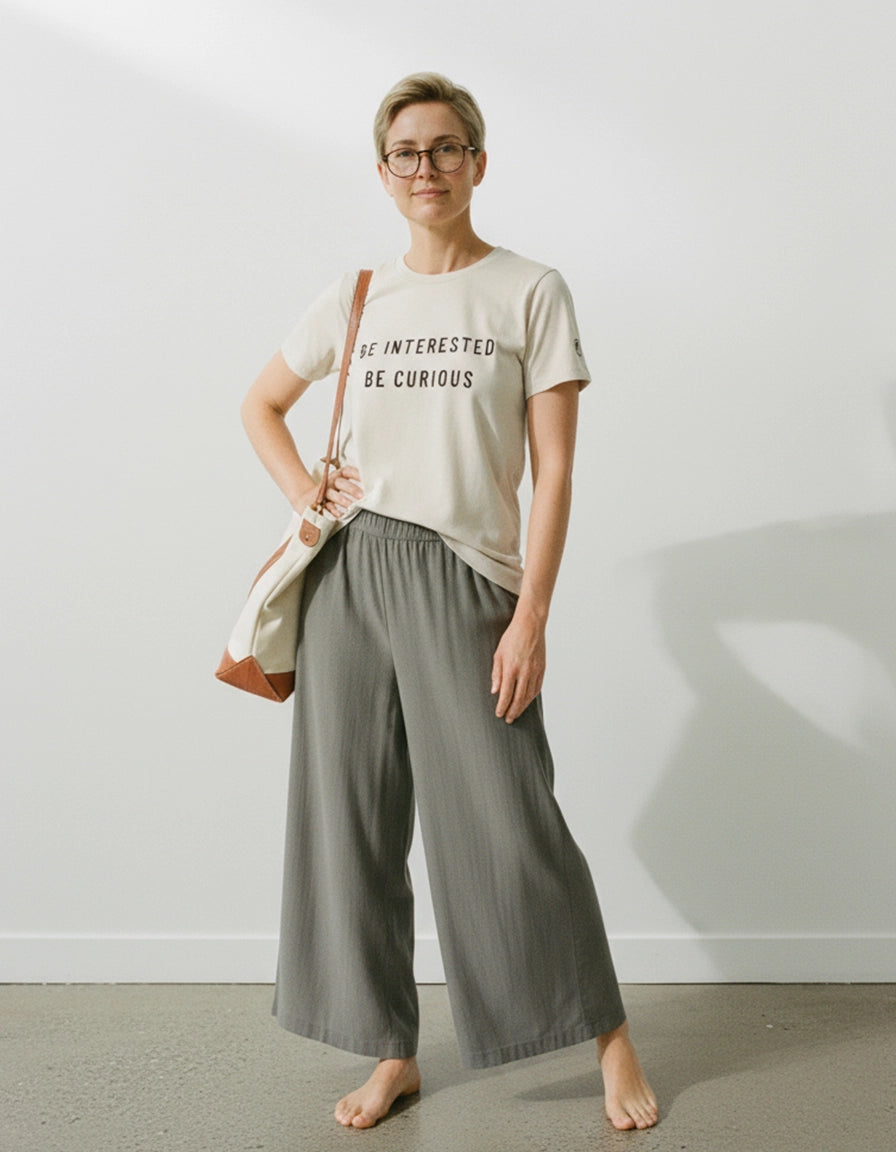 Person wearing a ponlo.com  t-shirt with text and wide-leg pants against a white wall.