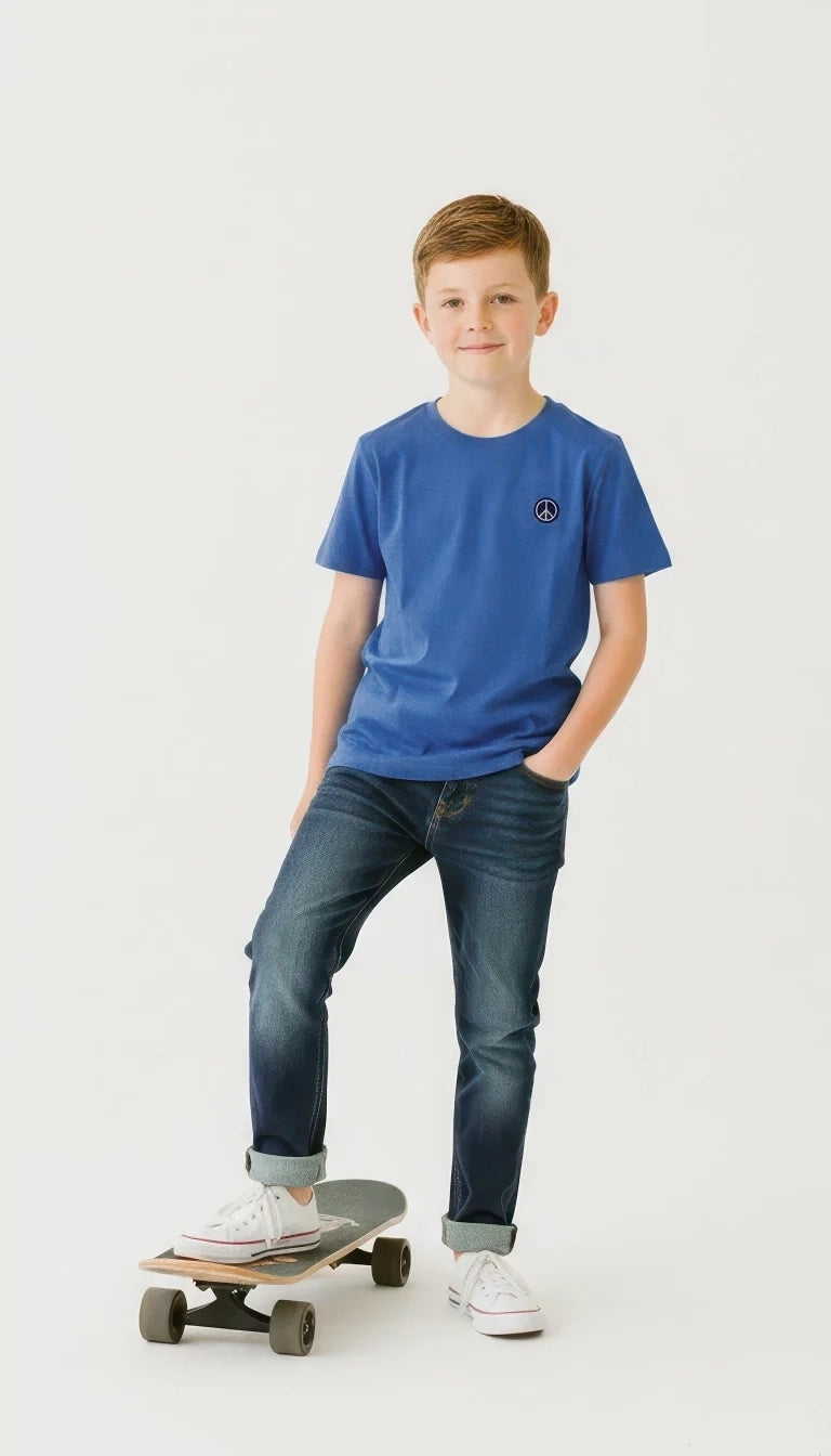Young boy in a blue t-shirt and jeans standing on a skateboard against a white background