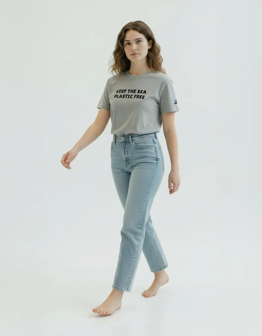 Person wearing a heather gray organic cotton t-shirt made by Ponlo with 'Keep the Sea Plastic Free' text on a white background. Wave patch on the left sleeve