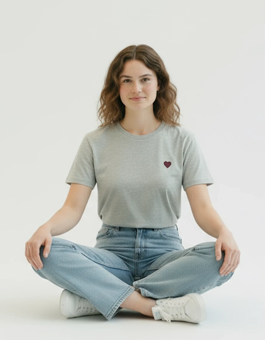 Woman sitting cross-legged wearing a gray ponlo.com t-shirt with a red heart and blue jeans on a white background