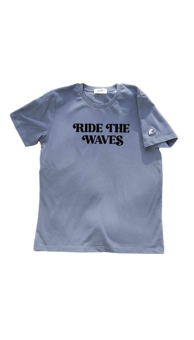 Blue Ponlo.com T-shirt featuring the bold black text “RIDE THE WAVES” across the chest and a small embroidered wave patch on the left sleeve, displayed on a transparent background.