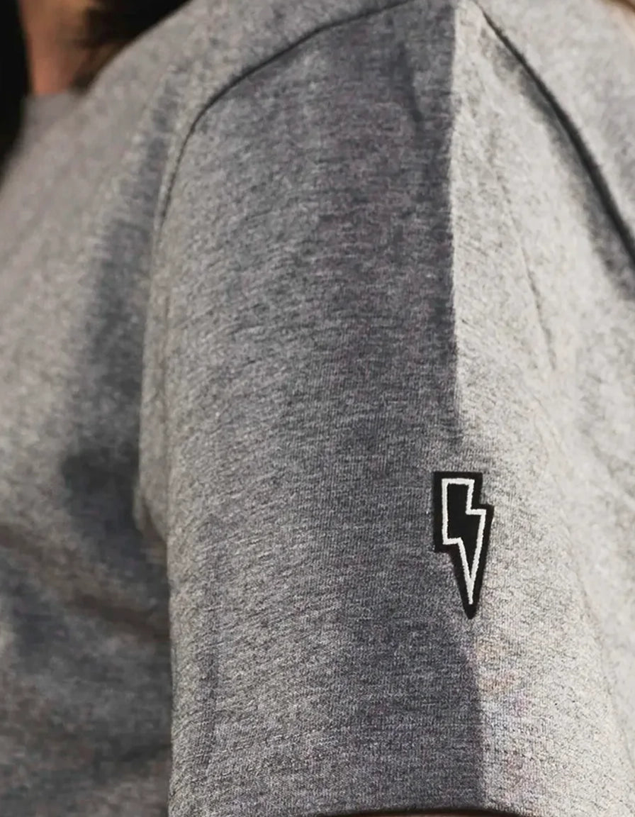 Close-up of a gray sleeve ponlo.com t-shirt with a black lightning bolt embroidered patch.